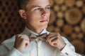 Close-up portrait of young male businessman is getting dressed for work. A blond guy in a white shirt is trying on a bow