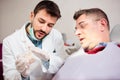 Young male dentist showing gum and teeth model to mature man, consulting