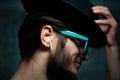 Close-up portrait of young man, listen the music with wireless earphones, wearing blue sunglasses and black hat. Royalty Free Stock Photo