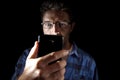 Close up portrait of young man looking intensively to mobile phone screen with blue eyes wide open isolated on black background