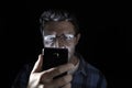 Close up portrait of young man looking intensively to mobile phone screen with blue eyes wide open isolated on black background Royalty Free Stock Photo