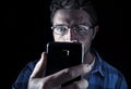 Close up portrait of young man looking intensively to mobile phone screen with blue eyes wide open isolated on black background