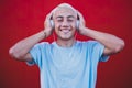 Close up and portrait of young man or millennial hearing and listening music having fun smiling with a red colorful wall at the