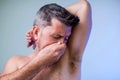 Close up portrait of man, smelling his armpit, feeling bad odor, wants to take a shower, needs antiperspirants