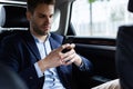 Close up portrait of young man in suit holding smartphone while sitting on the back seat of the car. Handsome young Royalty Free Stock Photo