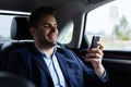 Close up portrait of young man in suit holding smartphone while sitting on the back seat of the car. Handsome young Royalty Free Stock Photo