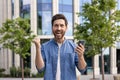 Close-up portrait of a young man who rejoices at the camera, shows a victory sign with his hands, holds a mobile phone Royalty Free Stock Photo