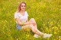 Close up portrait of young model blonde woman sitting on grass, posing in white casul t shirt and denim skirt, has romantic Royalty Free Stock Photo