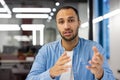 Close-up portrait of a young Muslim man sitting in a modern office and talking to the camera while gesturing with his Royalty Free Stock Photo
