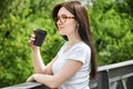 Close-up portrait young pretty woman drinking coffee from black paper cup sitting on a bridge in the park Royalty Free Stock Photo
