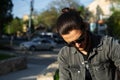 Close-up portrait of young serious guy, looking down; wearing sunglasses and shirt. Background of blurred street with copy space. Royalty Free Stock Photo