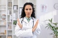 Close-up portrait of young serious hispanic female doctor standing in hospital office in white coat and crossed arms Royalty Free Stock Photo