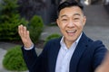 Close-up portrait of a young smiling Asian businessman man standing outside and talking on video with a camera in his Royalty Free Stock Photo