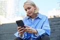 Close up portrait of young stylish female model, sitting outdoors on stairs, using mobile phone, reading on smartphone Royalty Free Stock Photo