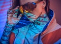 Close up portrait of a young tattooed racer woman posing in a vivid neon studio over text projection