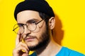 Close-up portrait of young thoughtful  hipster man wearing round eyeglasses and beanie hat on background of yellow color. Royalty Free Stock Photo