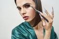 Close up portrait of young transgender holding brush and looking at camera while applying dark night party makeup