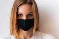 Close-up portrait of a young woman in a black medical mask and blue eyes and white T-shirt on white background. Royalty Free Stock Photo