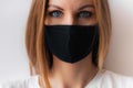 Close-up portrait of a young woman in a black medical mask and blue eyes and white T-shirt on white background. Royalty Free Stock Photo