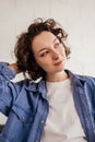 Close-up portrait of young woman with short curly hair in blue shirt standing in front of white wall looking away Royalty Free Stock Photo
