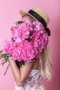 Close-up portrait of young woman in summer dress and straw hat holding peonies bouquet over her shoulder Royalty Free Stock Photo