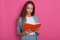 Close up portrait of young women reading something in notebook isolated over rosy background, looks concentrated, looking down, Royalty Free Stock Photo