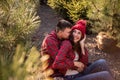 Close-up portraits of young couple in red checkered shirts sitting among Christmas tree seedlings