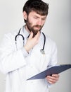 Close-up portret of a Doctor holding a map-case for note, stethoscope around his neck. He rubs his chin. different Royalty Free Stock Photo