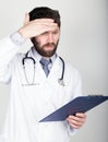 Close-up portret of a Doctor holding a map-case for note, stethoscope around his neck. He wipes his forehead. different Royalty Free Stock Photo