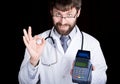 Close-up portret of a Doctor holding pos-terminal, stethoscope around his neck. he makes an OK sign with your fingers Royalty Free Stock Photo