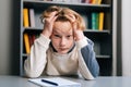 Close-up portriat of exhausted pupil boy tired from studying holding head head with hands while sitting at desk