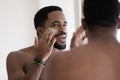 Close up positive African American young man applying face cream