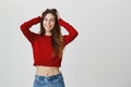 Close up of positive caucasian female student with dark hair in red cropped sweater and casual jeans smiling with teeth