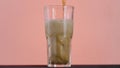 Close up of pouring cola in a long transparent glass with Ice and bubbles. Action. Soda soft drink isolated on pink wall Royalty Free Stock Photo