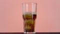 Close up of pouring cola in a long transparent glass with Ice and bubbles. Action. Soda soft drink isolated on pink wall Royalty Free Stock Photo