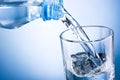 Close-up pouring water from bottle into glass on blue backgrou