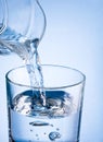 Close-up pouring water from a jug into glass on a blue background Royalty Free Stock Photo