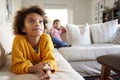 Close up of pre-teen girl lying on sofa watching TV in the living room, her younger brother sitting in the background, focus on fo