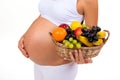 Close-up of a pregnant belly and a basket of exotic fruits.