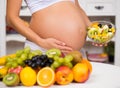 Close-up of a pregnant belly with fresh fruit and plate of salad. Royalty Free Stock Photo