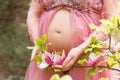 Close up of a pregnant belly and holding a branch with magnolia flowers in hands.
