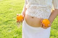 Close up pregnant belly holding oranges in hand