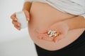 Close up on pregnant belly with medicine..Woman expecting a baby dressed in white holding pills. Taking drugs or vitamins during Royalty Free Stock Photo