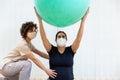 Close up of a pregnant woman with face mask sitting on floor doing pilates exercises with a ball with physiotherapist Royalty Free Stock Photo