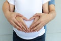 Close up pregnant wife and her husband showing heart with hands on color background. Royalty Free Stock Photo