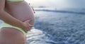 Close up of pregnant woman belly wearing yellow bikini on the beach. Royalty Free Stock Photo