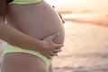 Close up of pregnant woman belly wearing yellow bikini on the beach at sunset. Royalty Free Stock Photo