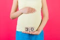 Close up of pregnant woman in colorful home clothing holding cubes with numbers of pregnancy weeks. Thirty weeks of pregnancy