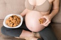 Close up of pregnant woman enjoys eating cookies resting on the sofa at home. Unhealthy sweet pastry during pregnancy concept