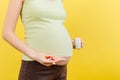 Close up of pregnant woman holding a bottle and a pile of pills in hands at colorful background with copy space. Healthcare